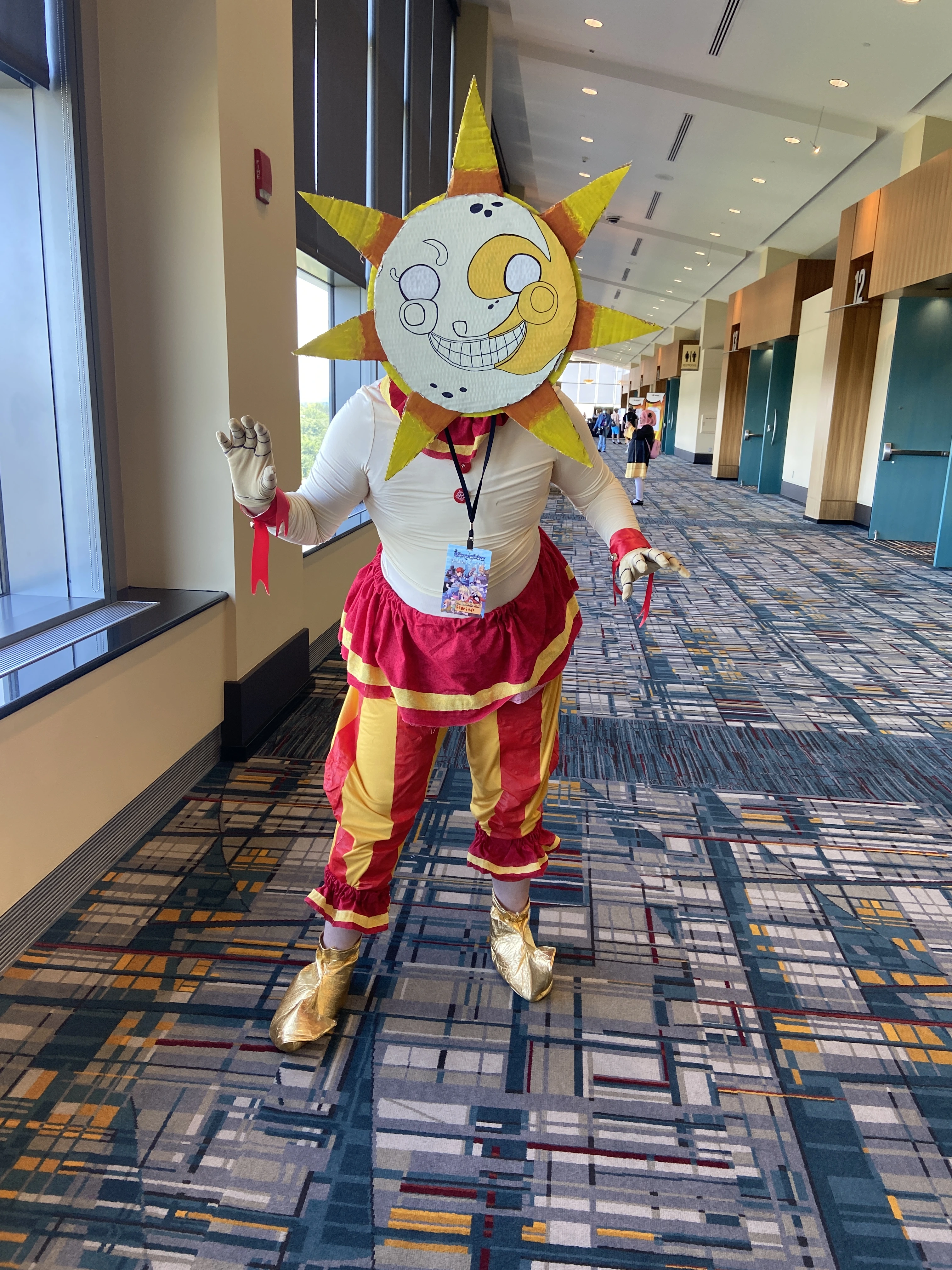 Me wearing a sun costume with a painted cardboard mask and red and yellow clown outfit.